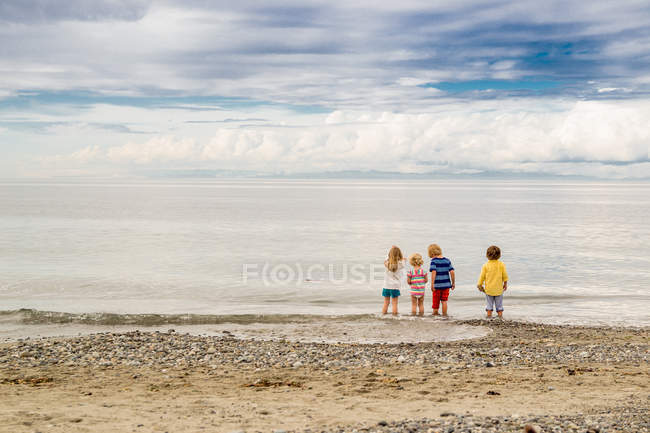 Rear view of four children standing on the beach — Stock Photo