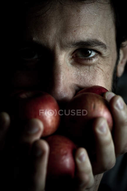 Человек держит яблоки перед лицом — стоковое фото
