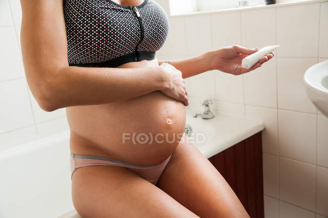 Mujer embarazada frotando crema hidratante - foto de stock