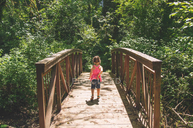 Jeune fille marchant à travers le pont dans les bois — Photo de stock