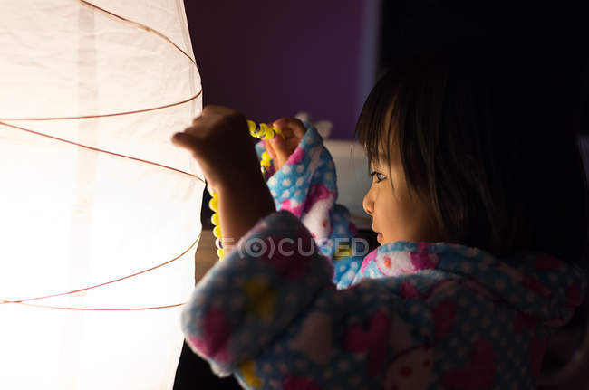 Girl standing by lamp and holding necklace — Stock Photo