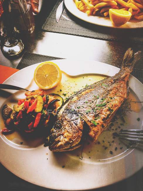 Рыба на тарелке с овощами — стоковое фото