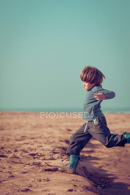 Мальчик играет и прыгает на пляже — стоковое фото