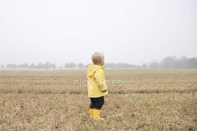 Niño en el campo en ropa de lluvia - foto de stock