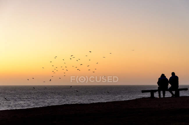 Deux silhouettes sur la plage au coucher du soleil — Photo de stock