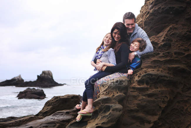 Sonriente familia sentada en las rocas - foto de stock