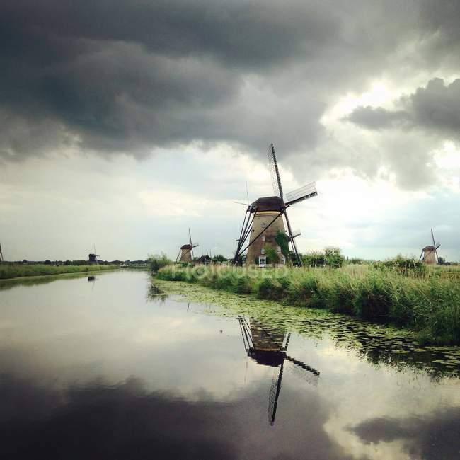 Windmills on grassy riverbank — Stock Photo