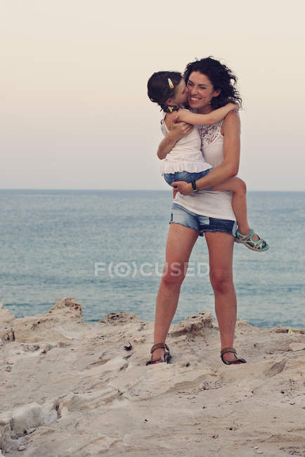 Madre abrazando hija en la playa - foto de stock