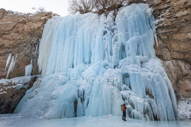 Backpacker standing under frozen waterfall — Stock Photo