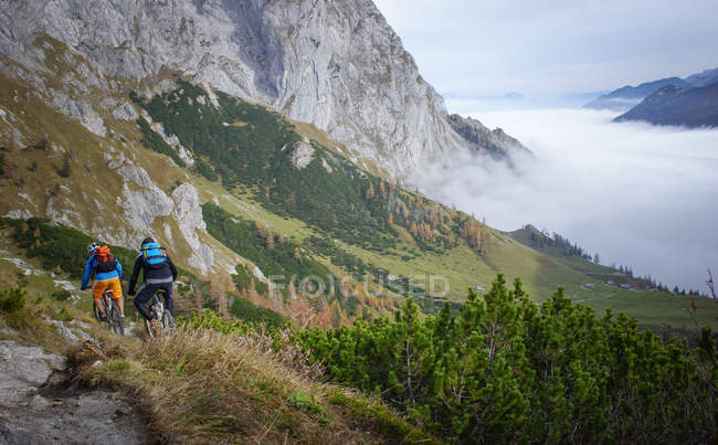 Two mountain bike riders descending into valley — Stock Photo