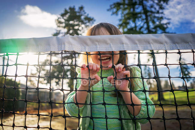 Fille se cachant derrière le filet de tennis — Photo de stock