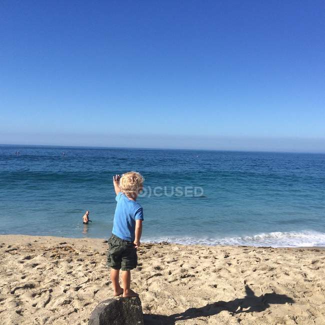 Мальчик, стоящий на камне на пляже — стоковое фото