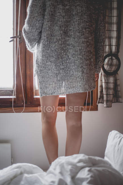Woman standing on bed looking out of window — Stock Photo
