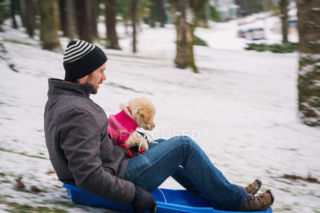 Man sitting on sledge with puppy dog — Stock Photo
