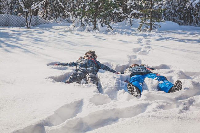 Menino e menina fazendo anjos de neve — Fotografia de Stock