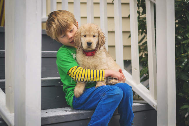 Niño sentado en el sofá con cachorro perro - foto de stock