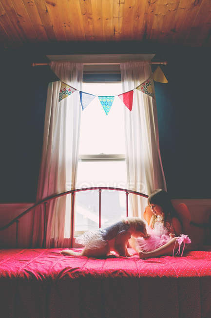 Mädchen sitzt auf Bett und spielt mit Hund — Stockfoto