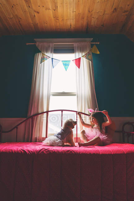 Chica sentada en la cama y jugando con el perro - foto de stock