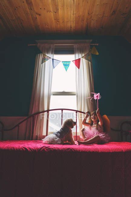 Menina sentada na cama e brincando com o cão — Fotografia de Stock