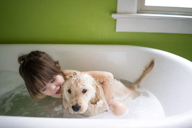 Girl sitting in bath with puppy dog — Stock Photo