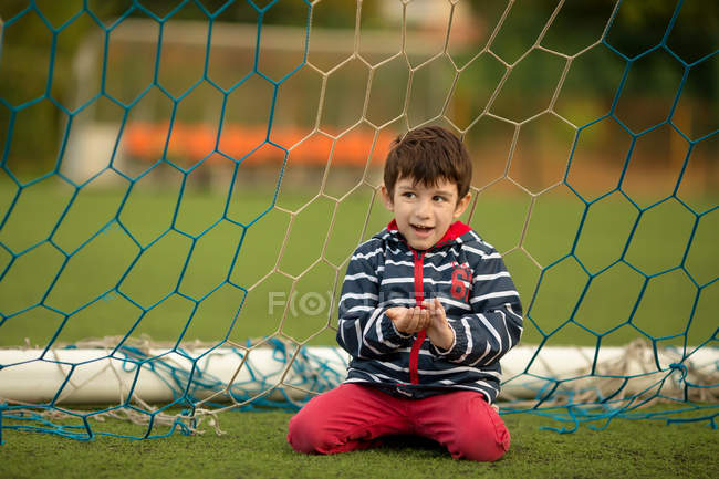 Menino sentado na frente do gol de futebol — Fotografia de Stock