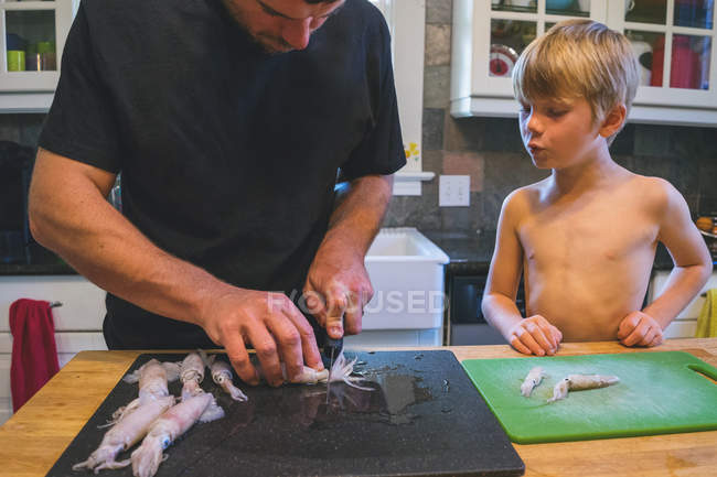 Хлопчик дивиться, як людина прибирає кальмари — стокове фото
