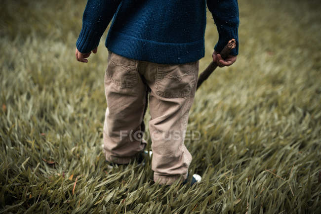 Criança no campo segurando pau de madeira — Fotografia de Stock