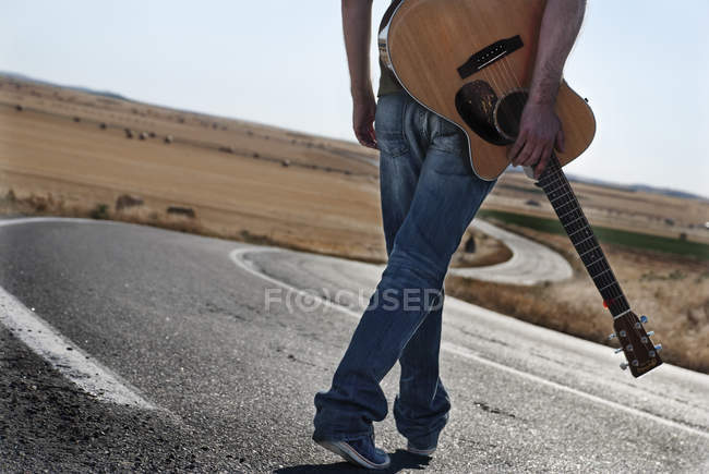 Homem andando estrada abaixo com guitarra — Fotografia de Stock