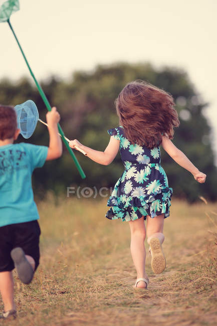 Menino e menina perseguindo borboletas — Fotografia de Stock