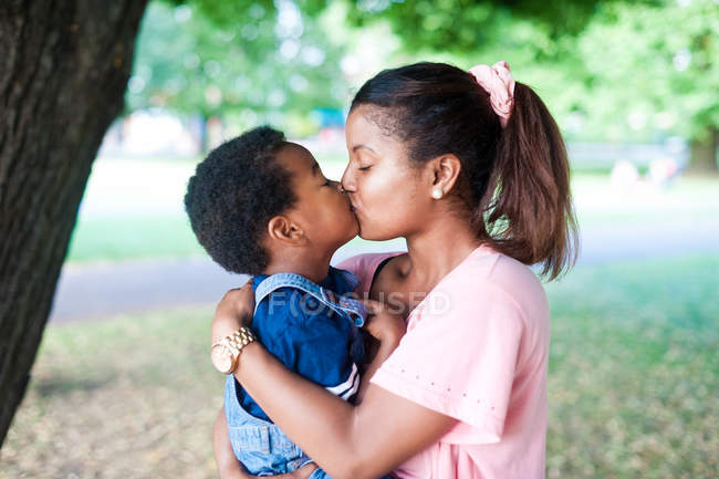 Mulher dando a seu filho um beijo no parque — Fotografia de Stock