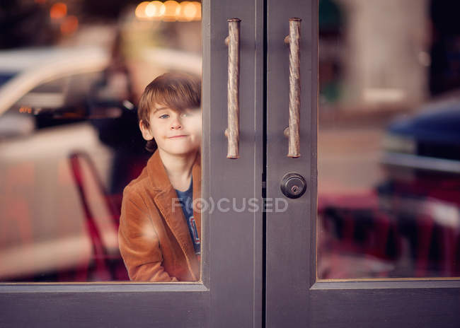 Chico mirando a través de puertas de vidrio - foto de stock