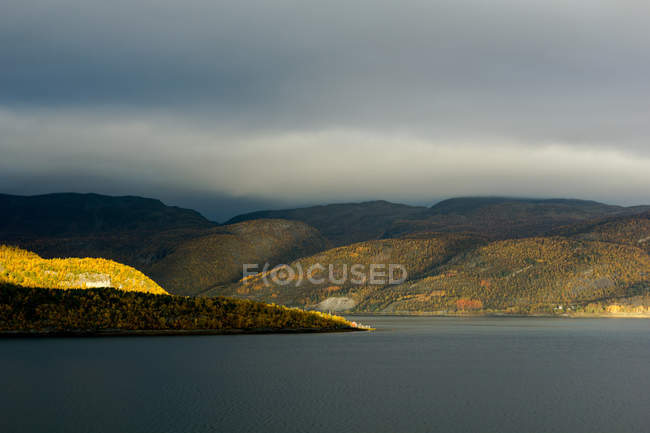 Paesaggio con lago, colline e cielo coperto — Foto stock