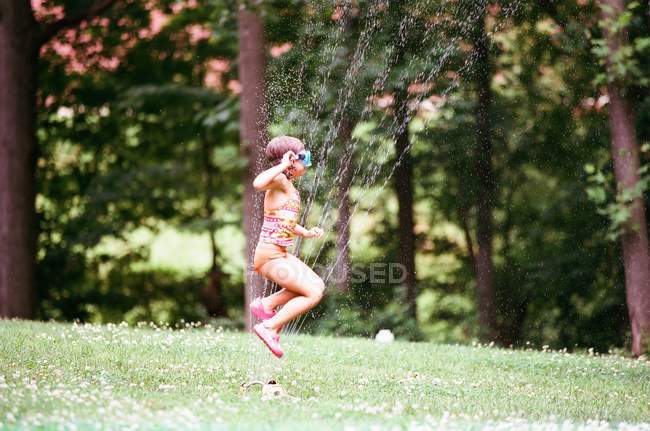 Menina pulando no aspersor — Fotografia de Stock