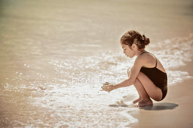 Girl crouching by water edge on beach — Stock Photo