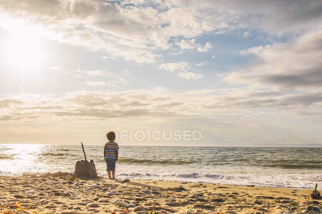 Niño al lado del castillo de arena - foto de stock
