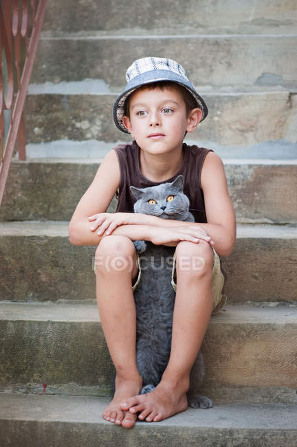 Мальчик сидит на ступеньках с котом — стоковое фото