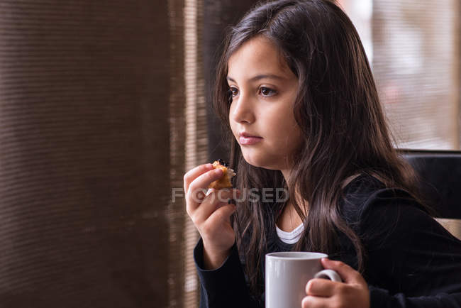 Little girl eating cake and holding mug — Stock Photo