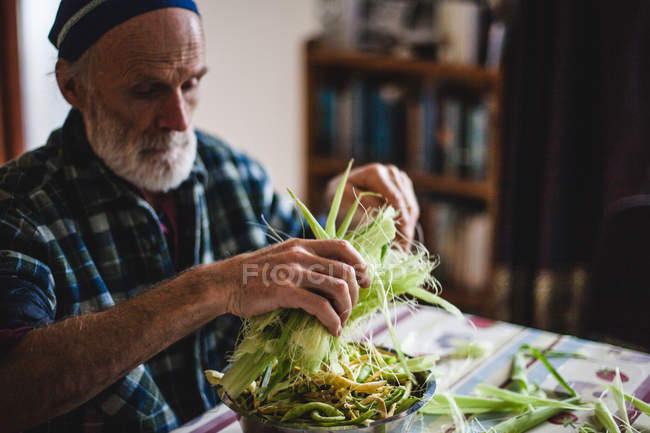 Старший чоловік готує свіжу кукурудзу — стокове фото