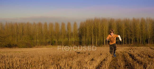 Boy running through tree lined field — Stock Photo