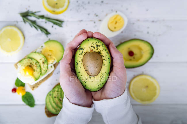 Hände, die eine halbe Avocadofrucht halten — Stockfoto