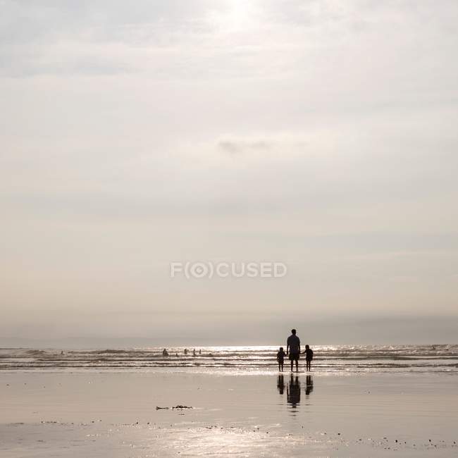 Hombre de pie en la playa con niños - foto de stock