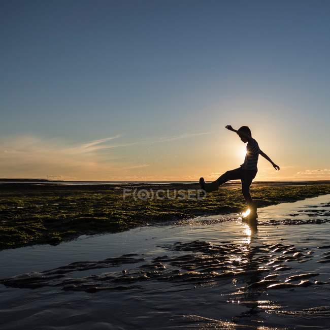 Little boy kicking water at beach — Stock Photo