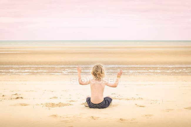 Мальчик сидит на пляже и медитирует — стоковое фото