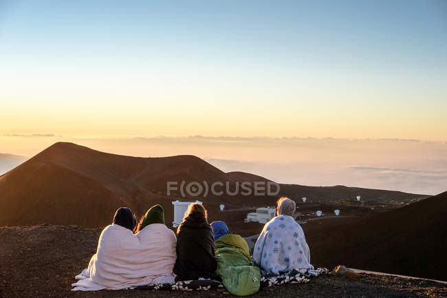 Les gens enveloppés dans des couvertures regardant le coucher du soleil — Photo de stock