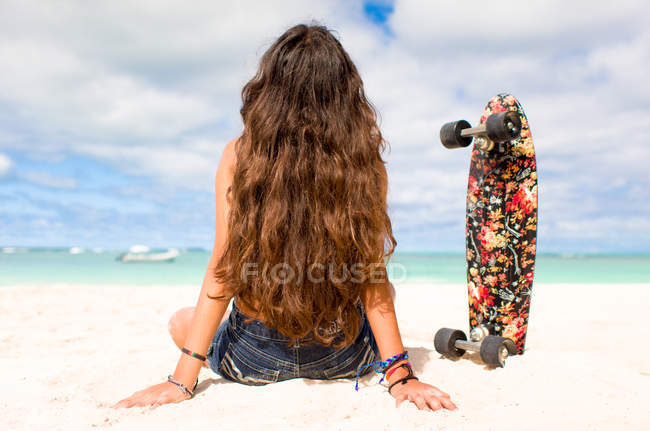 Дівчина сидить на піщаному пляжі зі скейтбордом — стокове фото