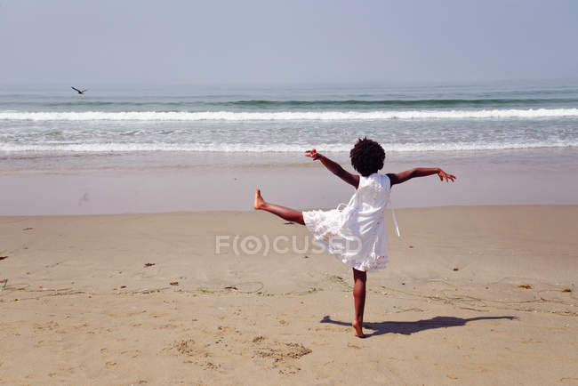 Girl standing on one leg on beach — Stock Photo