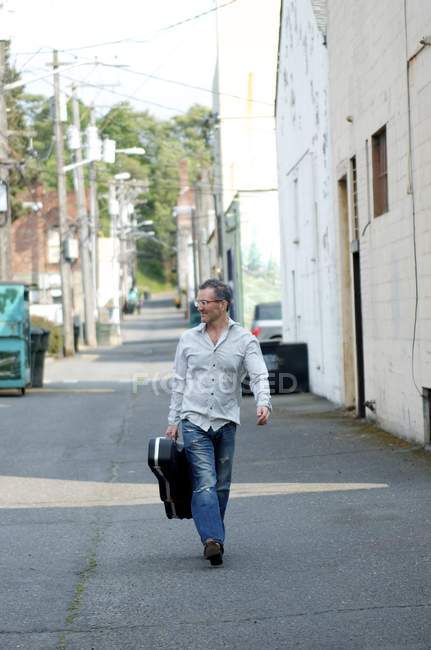 Homme avec étui de guitare marchant dans l'allée — Photo de stock