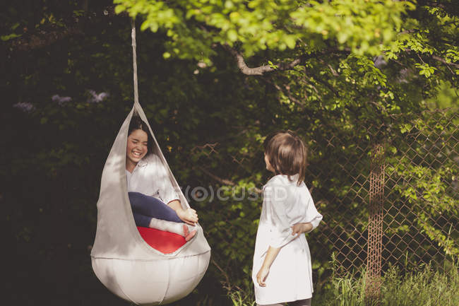 Girl in hanging chair talking to boy — Stock Photo