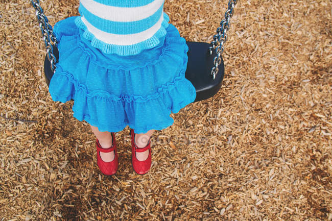 Fille assise sur balançoire dans le parc sur aire de jeux — Photo de stock