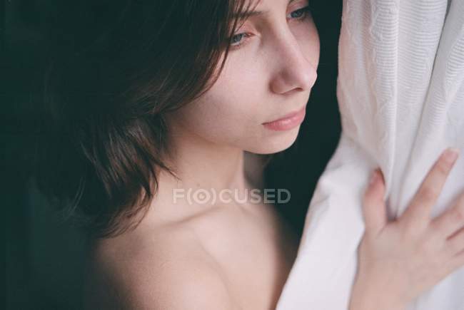 Woman looking out from behind curtains — Stock Photo